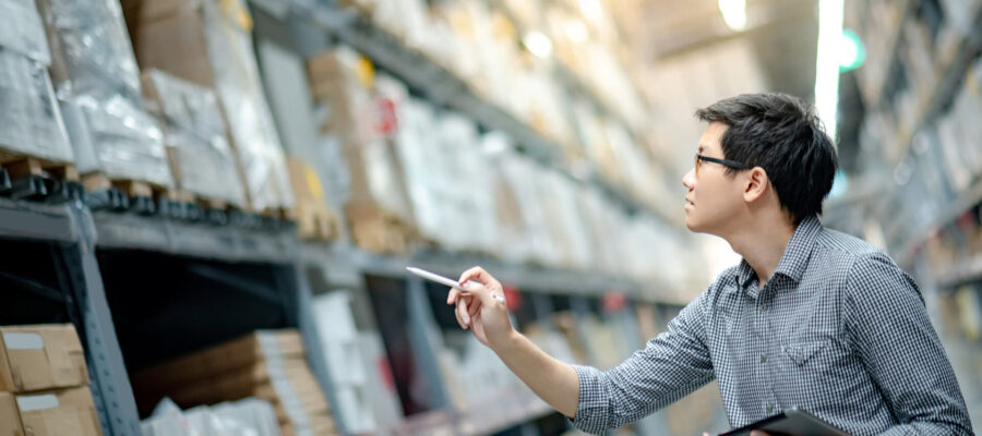 Asiatischer Mann bei der Inventur mit einem Tablet im Lager